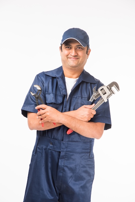 smiling indian plumber with pipe wrench or plumbing spanner, wearing blue uniform with cap showing thumbs up. isolated over white background